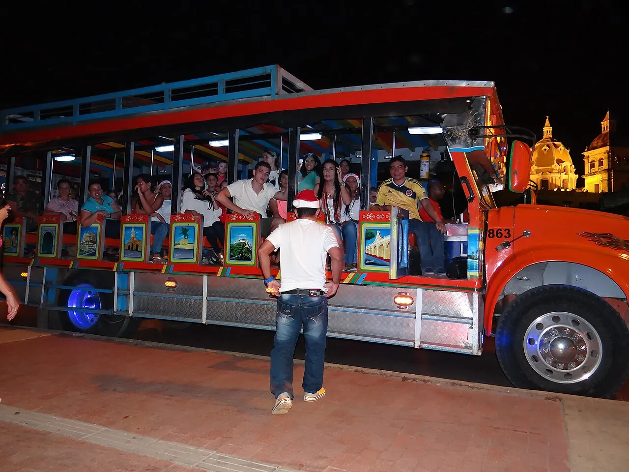 Grupo de turistas en una chiva de noche, con la cúpula de la catedral al fondo
