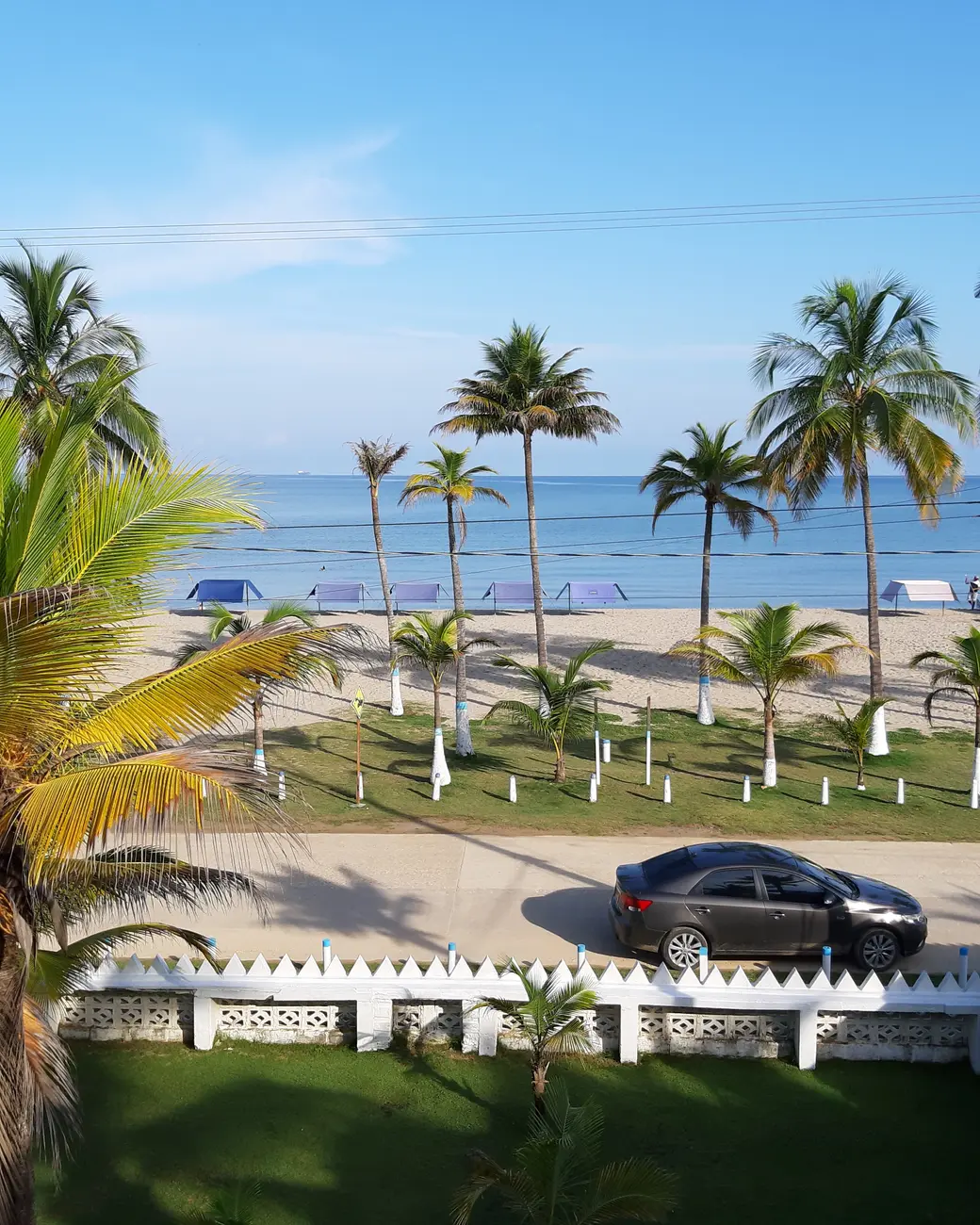 Playa de Coveñas vista desde lo alto, con palmeras, una calle con un carro estacionado y el mar azul del golfo de Morrosquillo al fondo.